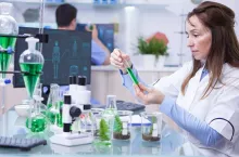 Side view of female scientist doing research on plants holding a green solution in a test tube. Female bioligist.