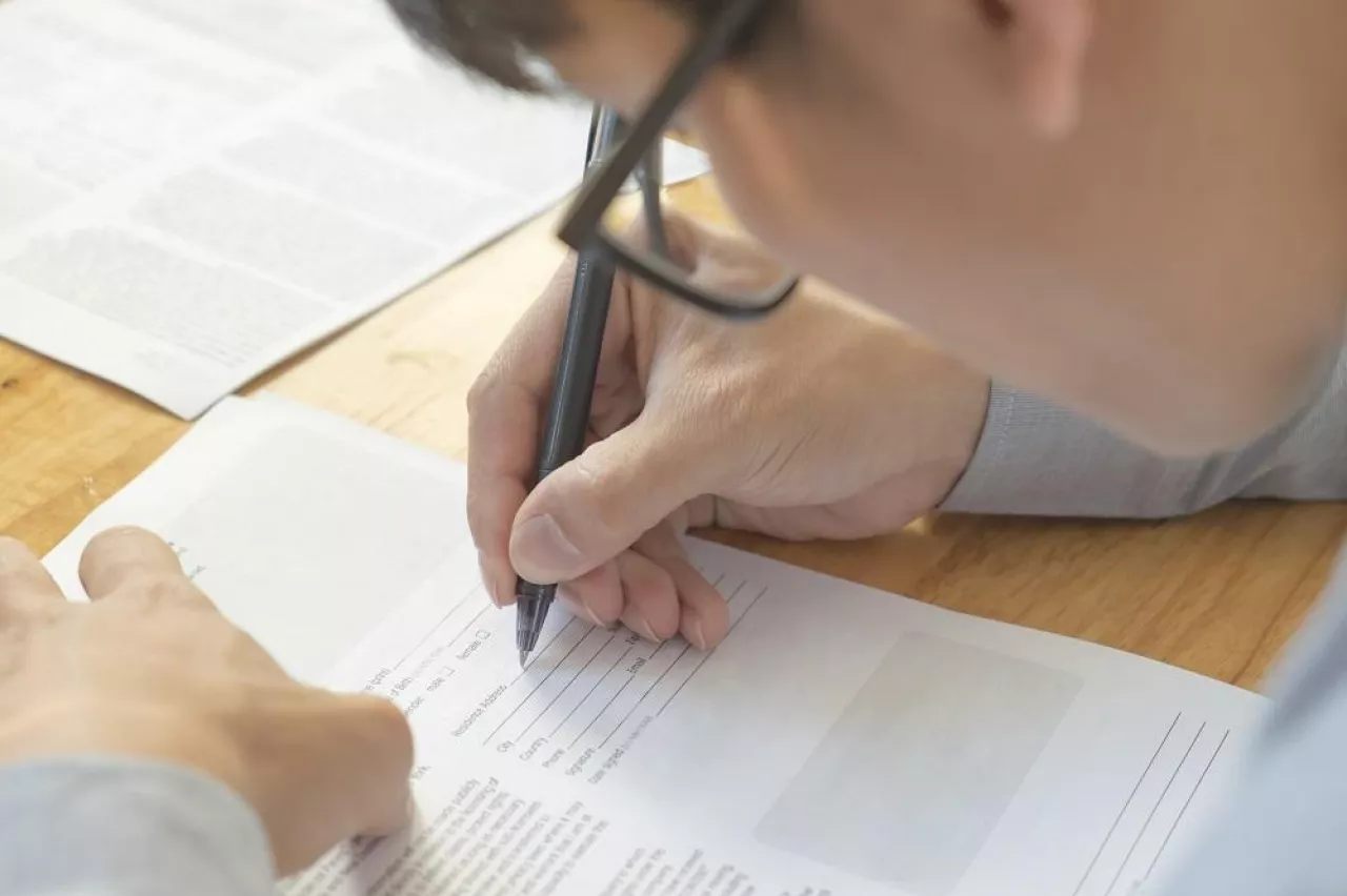 Man completing personal information on a application form. Select focus at hand and pen.