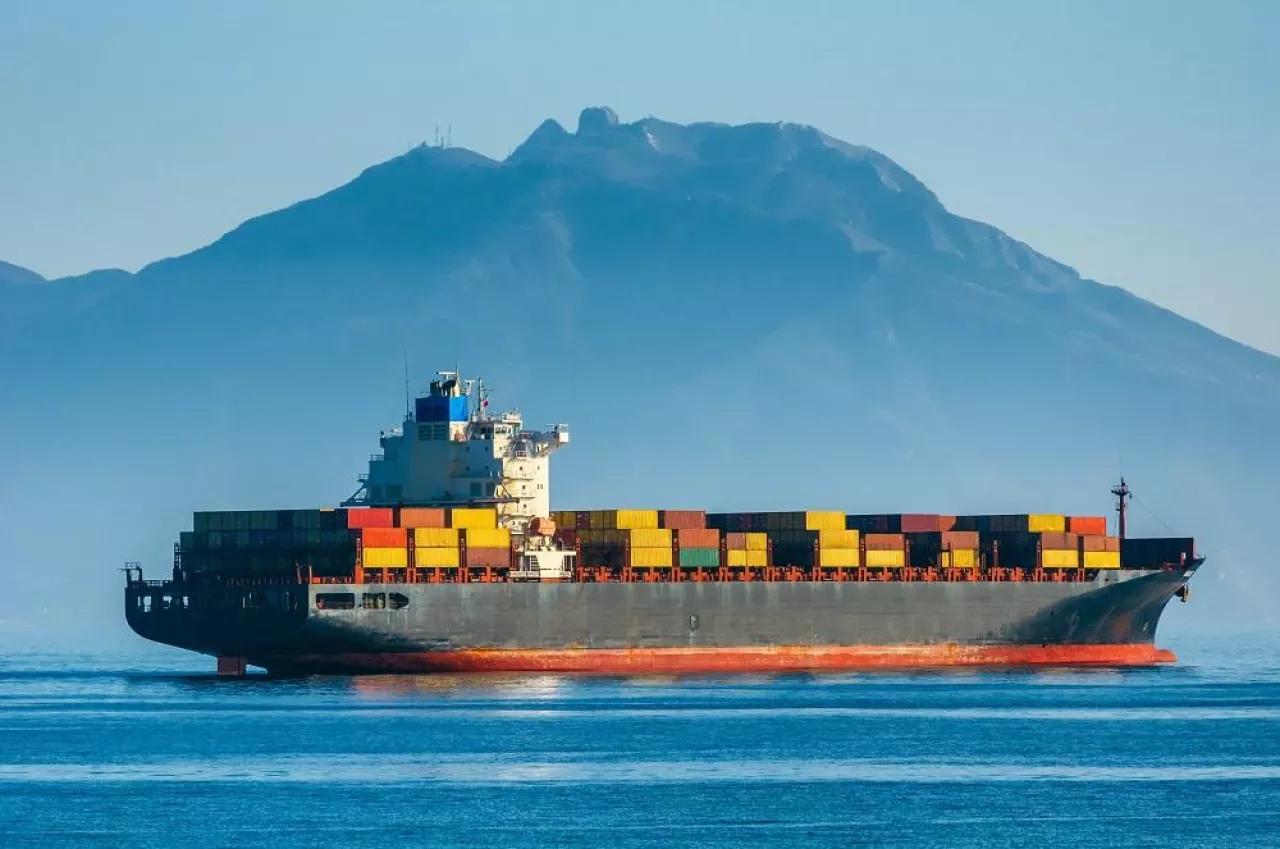 Container ship leaves the port on a background of mountains