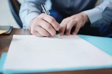 Business man at work in corporate office. Detail of hands of a busy manager signing documents and papers in a blue folder. Copy space.