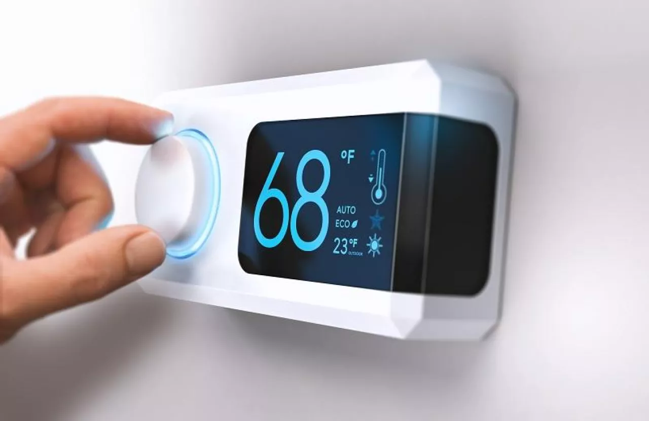 Hand turning a home thermostat knob to set temperature on energy saving mode. fahrenheit units. Composite image between a photography and a 3D background.