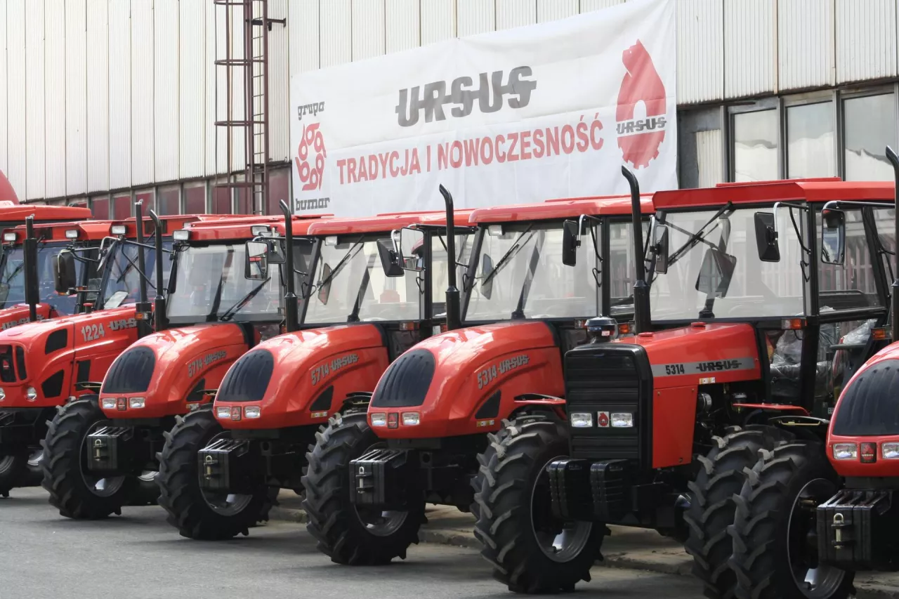 Różne modele ciągników marki Ursus stoją w rzędzie na placu przed budynkiem